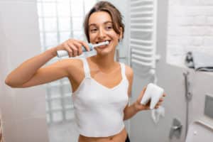 Young and cheerful woman brushing teeth with electric toothbrush during morning hygiene procedures in the bathroom